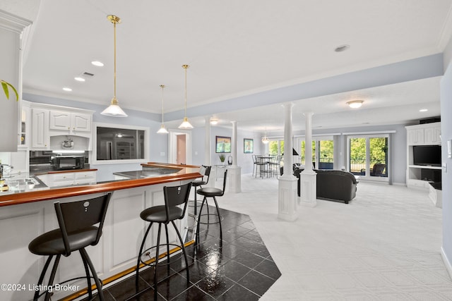 kitchen with a breakfast bar, open floor plan, white cabinets, black microwave, and ornate columns