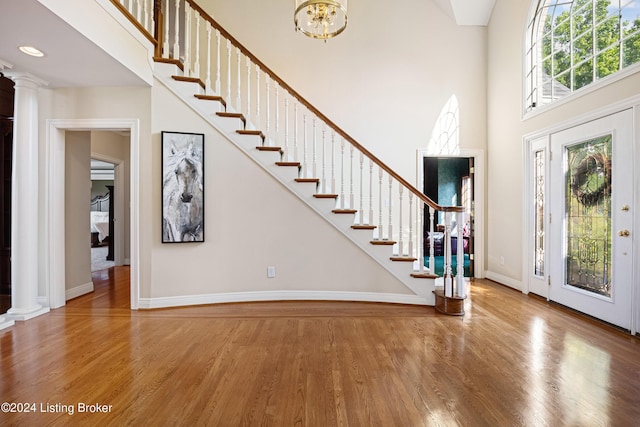 entryway featuring a high ceiling, wood finished floors, baseboards, stairs, and decorative columns