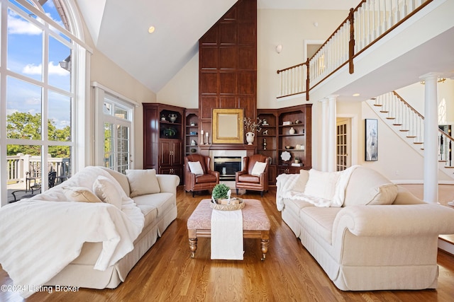 living area with stairs, a glass covered fireplace, decorative columns, and wood finished floors