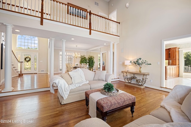 living area featuring ornate columns, visible vents, a high ceiling, wood finished floors, and baseboards