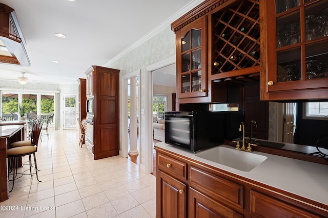 kitchen with light tile patterned floors, wall oven, a sink, ornamental molding, and glass insert cabinets