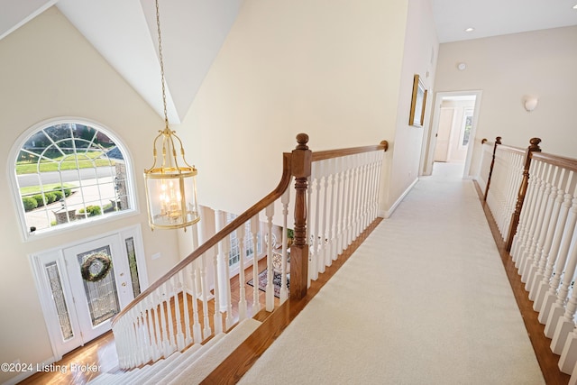 hallway featuring a chandelier, high vaulted ceiling, and an upstairs landing