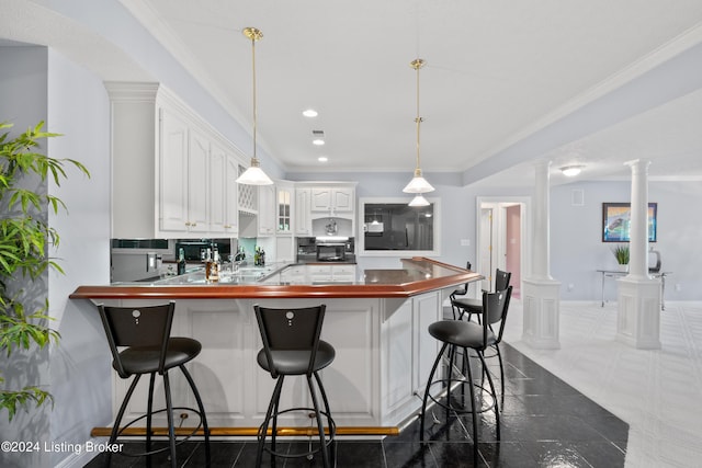 kitchen featuring a peninsula, white cabinetry, decorative columns, and crown molding