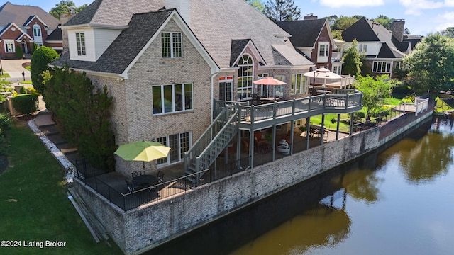 rear view of house featuring roof with shingles, brick siding, a deck with water view, a residential view, and stairs