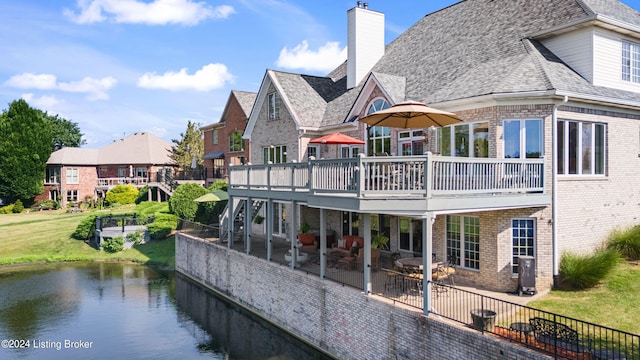 back of property featuring brick siding, a yard, a chimney, a patio area, and a deck with water view