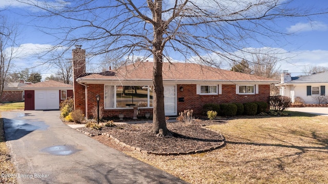 ranch-style home with an outbuilding, driveway, brick siding, and a chimney