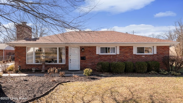 view of front facade featuring roof with shingles, a chimney, a front lawn, and brick siding