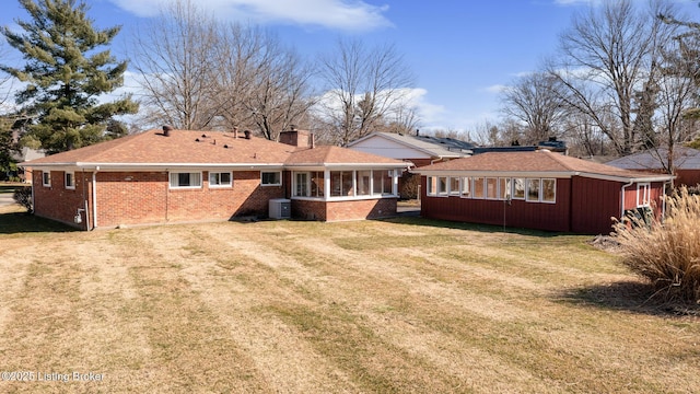 rear view of house with cooling unit, brick siding, a sunroom, a yard, and a chimney