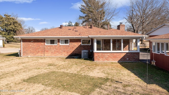 rear view of property featuring cooling unit, brick siding, a yard, and a chimney