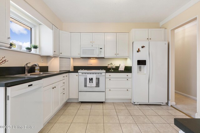 kitchen featuring dark countertops, white appliances, white cabinets, and a sink