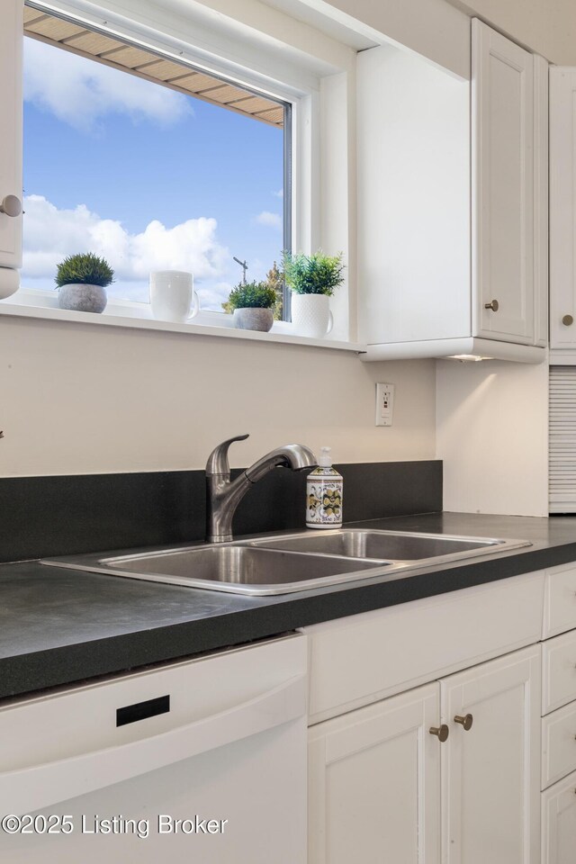 details with dark countertops, white dishwasher, white cabinets, and a sink