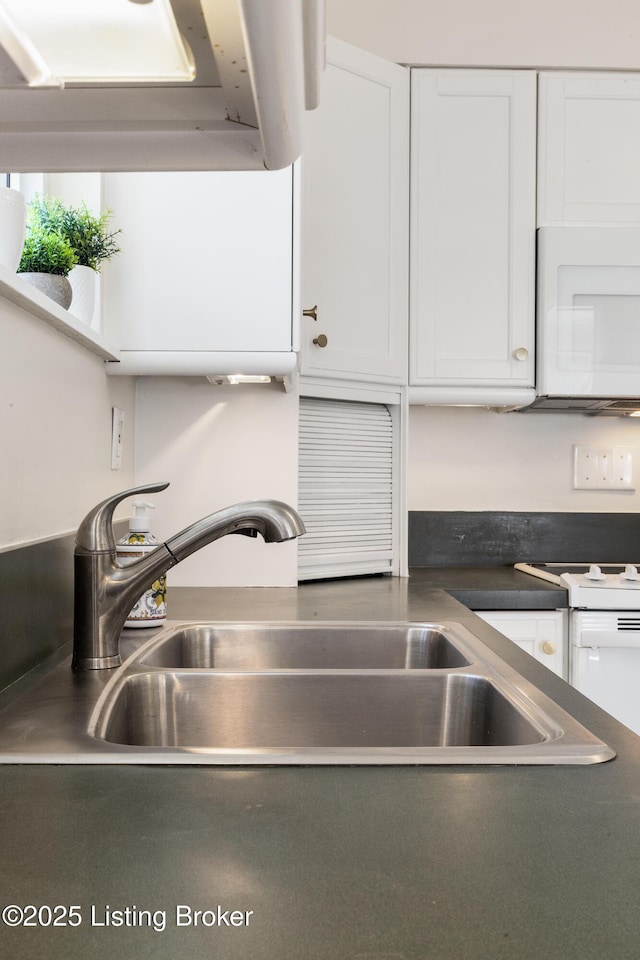 kitchen with white microwave, dark countertops, a sink, and white cabinets