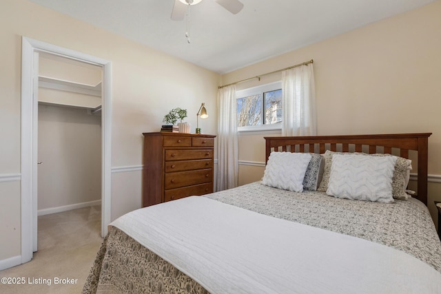 bedroom with a walk in closet, a closet, light colored carpet, a ceiling fan, and baseboards