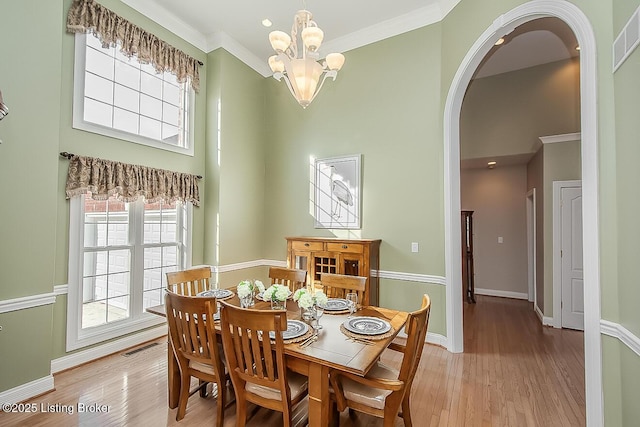 dining area with light wood-style flooring, arched walkways, and crown molding