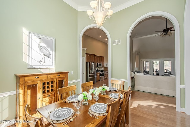 dining room with visible vents, arched walkways, light wood-style flooring, a high ceiling, and crown molding