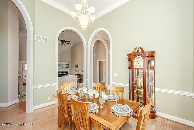 dining room with light wood-style floors, visible vents, arched walkways, and ceiling fan with notable chandelier