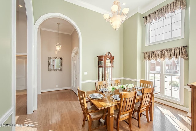 dining area featuring plenty of natural light, light wood-style flooring, arched walkways, and crown molding