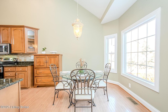 dining space featuring light wood-type flooring, high vaulted ceiling, visible vents, and baseboards