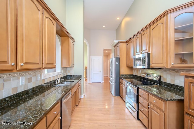 kitchen featuring a sink, appliances with stainless steel finishes, light wood-type flooring, decorative backsplash, and dark stone counters