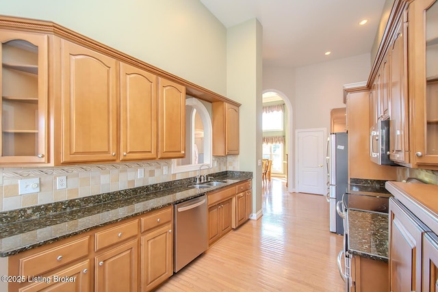 kitchen featuring arched walkways, backsplash, appliances with stainless steel finishes, a sink, and dark stone countertops