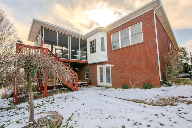 snow covered back of property featuring stairs, brick siding, and a sunroom