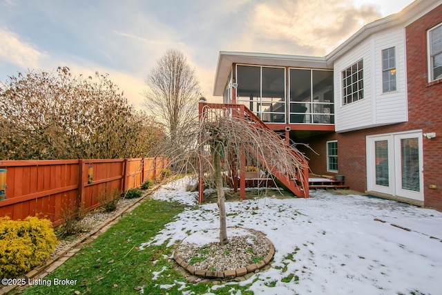 back of house at dusk with a sunroom, stairs, fence, and brick siding