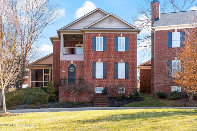 view of front facade featuring brick siding, a chimney, a front yard, a sunroom, and a balcony