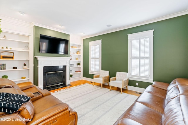 living area with built in features, baseboards, a fireplace with flush hearth, wood finished floors, and crown molding