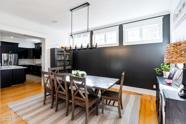 dining room featuring light wood finished floors, baseboards, visible vents, and crown molding