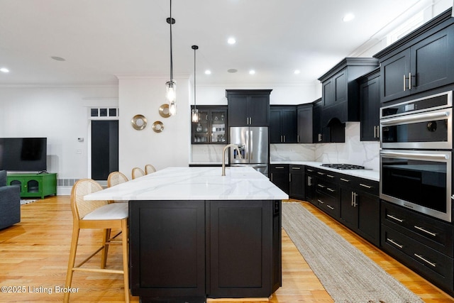 kitchen featuring decorative backsplash, light stone counters, appliances with stainless steel finishes, a kitchen breakfast bar, and dark cabinetry