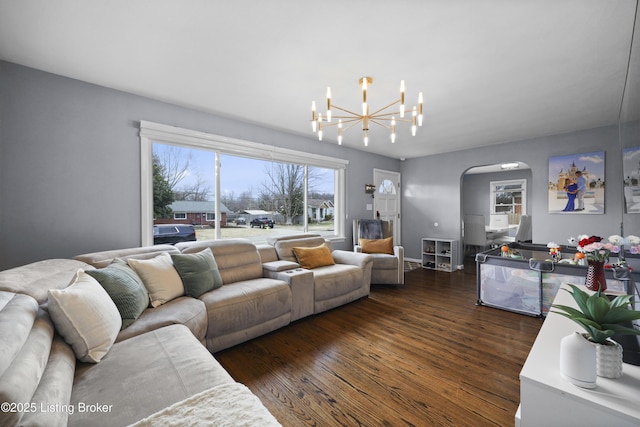 living area featuring arched walkways, dark wood finished floors, and a notable chandelier