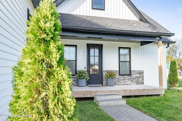 view of exterior entry featuring a shingled roof, stone siding, and a porch