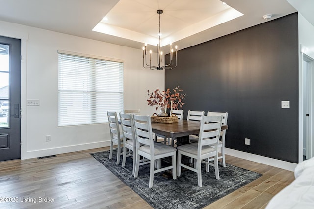 dining room with a notable chandelier, wood finished floors, visible vents, baseboards, and a tray ceiling