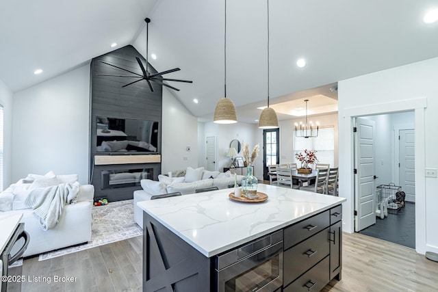 kitchen featuring light stone counters, open floor plan, hanging light fixtures, light wood-type flooring, and a center island