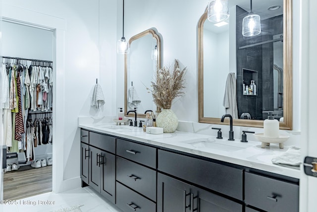 bathroom with a walk in closet, marble finish floor, a sink, and double vanity