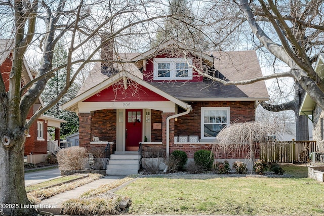 view of front of house featuring brick siding, fence, roof with shingles, a front lawn, and a chimney