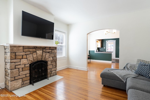 living area with arched walkways, a fireplace, wood finished floors, and baseboards