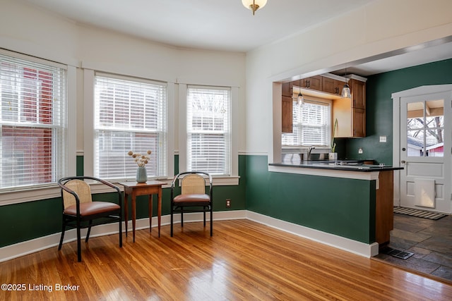 kitchen with a sink, wood finished floors, baseboards, brown cabinetry, and dark countertops