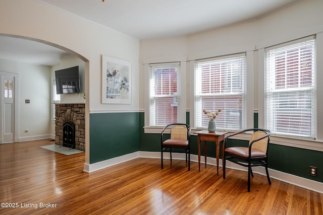 living area with arched walkways, a fireplace, baseboards, and wood finished floors