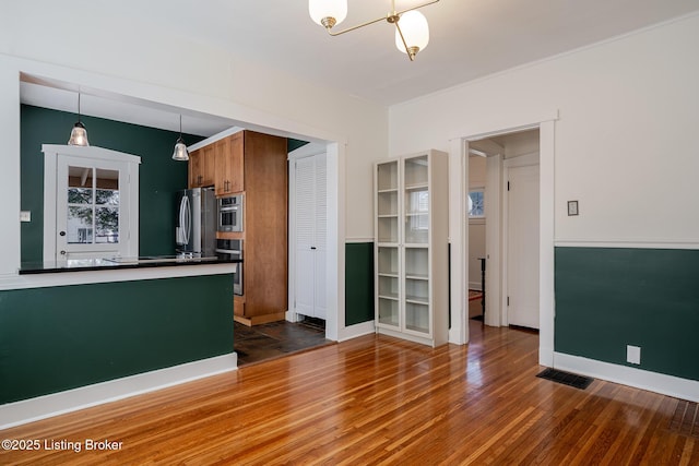 kitchen with visible vents, freestanding refrigerator, dark wood-style floors, brown cabinetry, and dark countertops