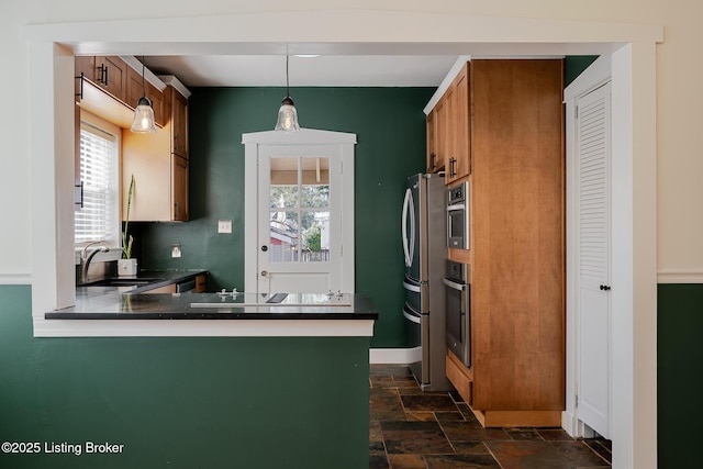 kitchen with stainless steel appliances, dark countertops, brown cabinetry, stone finish floor, and a sink