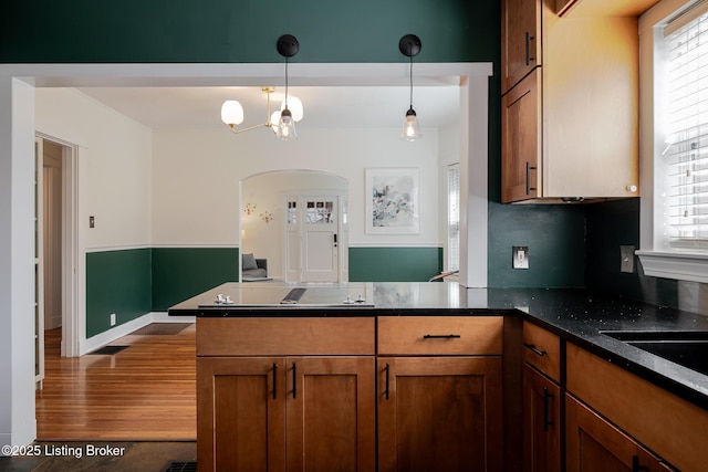 kitchen with hanging light fixtures, brown cabinets, plenty of natural light, and a peninsula