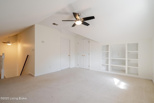 unfurnished room featuring lofted ceiling, light colored carpet, visible vents, baseboards, and built in features