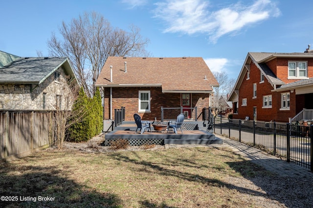 rear view of house featuring an outdoor fire pit, brick siding, a lawn, and fence