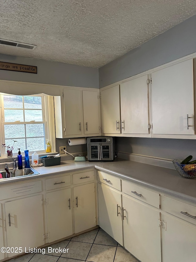 kitchen featuring light tile patterned floors, visible vents, light countertops, a sink, and a textured ceiling