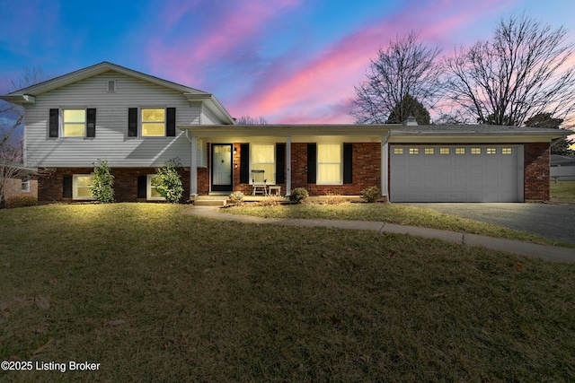 split level home featuring a garage, a front lawn, aphalt driveway, and brick siding