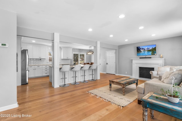 living area featuring light wood-style floors, a brick fireplace, baseboards, and recessed lighting