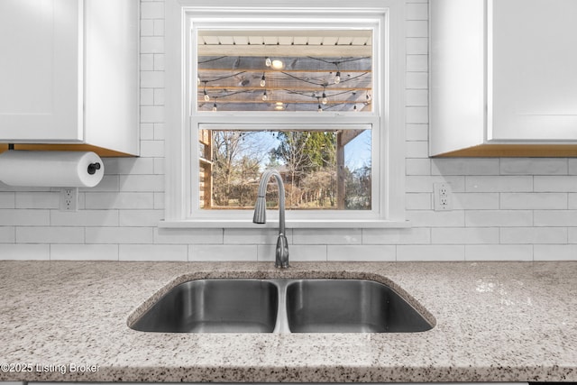 kitchen featuring light stone counters, decorative backsplash, white cabinets, and a sink