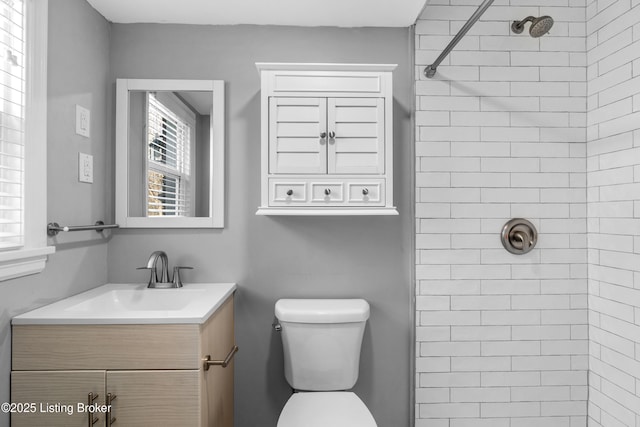 bathroom with toilet, tiled shower, and vanity