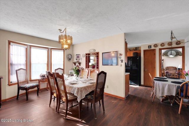 dining area featuring dark wood-type flooring, a textured ceiling, baseboards, and an inviting chandelier